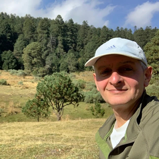 Mauricio Passaro al aire libre, sonriendo frente a un paisaje de bosque y cielo azul, representando conexión, serenidad y equilibrio interior.